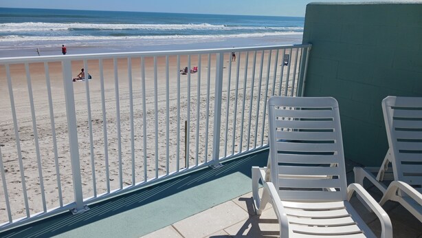 A balcony with white chairs overlooking a beach.