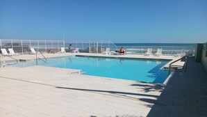 A swimming pool with a tiled deck, sun loungers, and a view of the ocean.