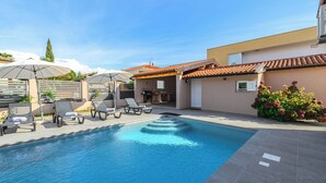 A swimming pool with lounge chairs and umbrellas, a building with a tiled roof, and a garden with flowers. - Villa with pool, air conditioning, internet and covered terrace, near the sea (Umag)