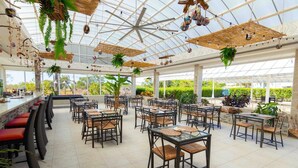 A spacious outdoor restaurant with multiple tables and chairs, a glass ceiling, and various hanging plants. - Villa Royale Luxury 4-bedroom Paradise In Sosua (Sosúa)