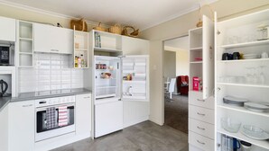 Een moderne keuken met witte kasten, een inbouwoven en een koelkast met open deuren waar diverse etenswaren in staan.