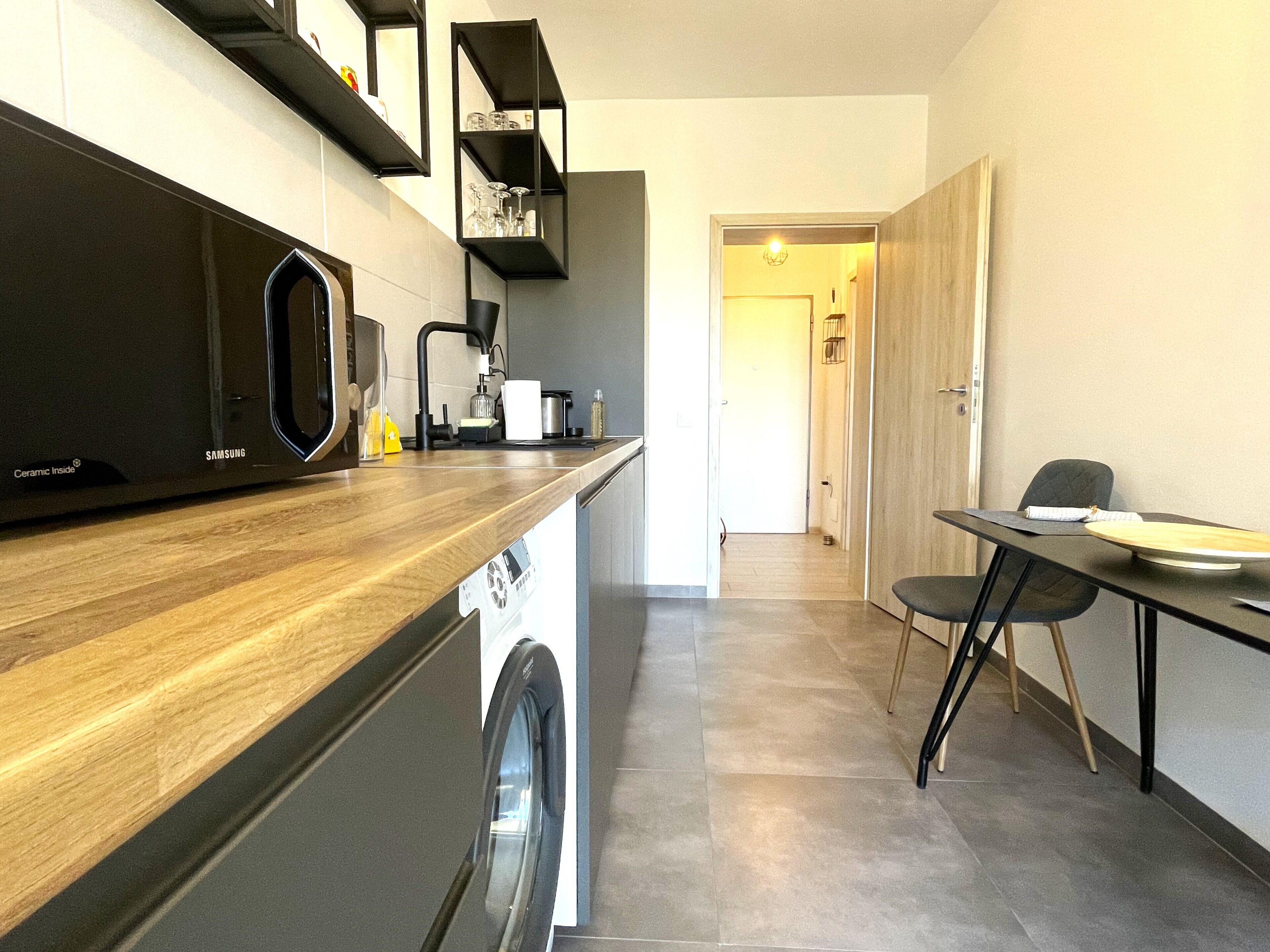 A modern kitchen with a washing machine, a coffee maker, and a dining area with a table and chairs.