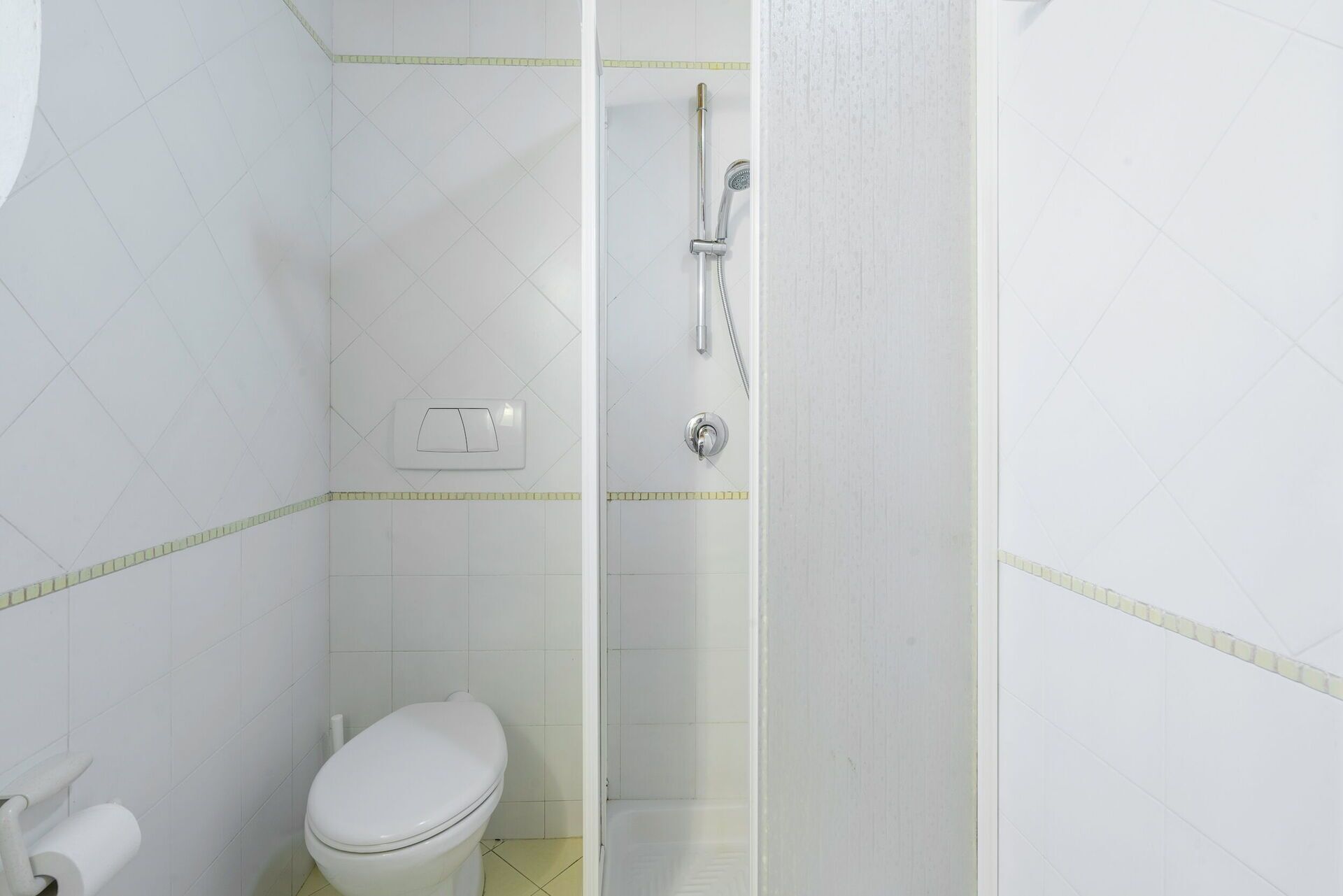 A small, white bathroom with a toilet, a shower, and a wall-mounted light switch.