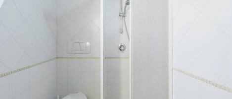 A small, white bathroom with a toilet, a shower, and a wall-mounted light switch.