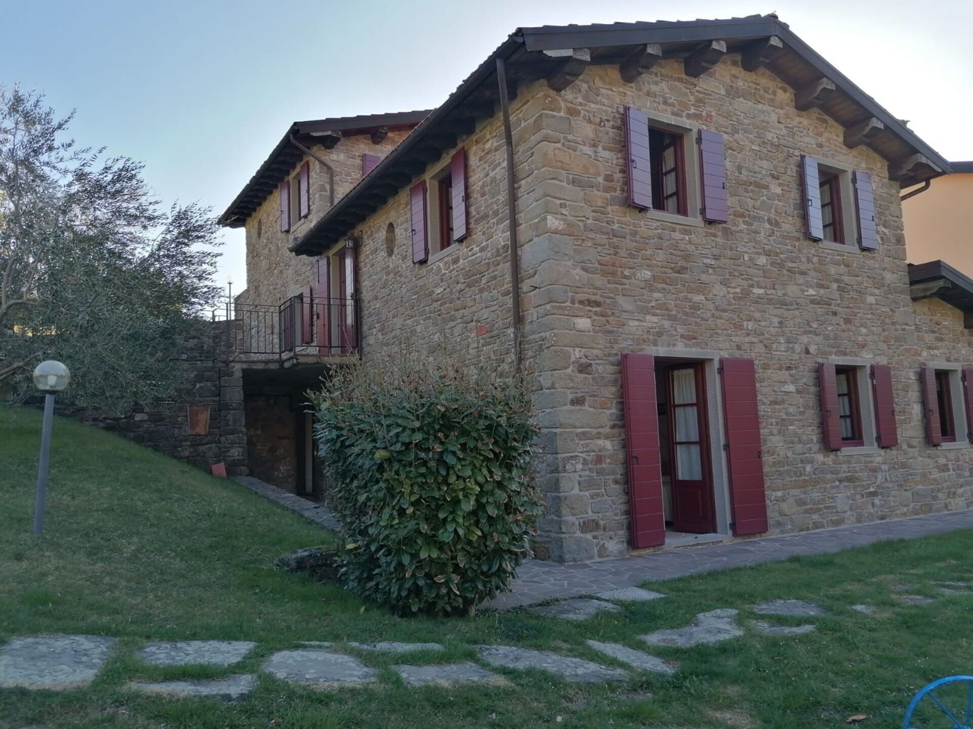 Un edificio de piedra con contraventanas rojas, un balcón y un pequeño jardín.