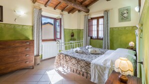 Un dormitorio con techo de madera, una cama con ropa de cama estampada, un aparador y una ventana con cortinas.