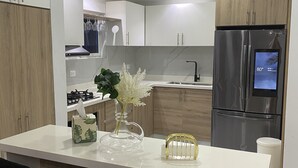 Une cuisine moderne avec des meubles blancs, un réfrigérateur en acier inoxydable et un îlot central agrémenté d’un vase et d’une boîte à mouchoirs.