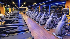Une salle de sport avec plusieurs rangées de vélos d’appartement et de tapis de course, un plancher en bois et un éclairage bleu.