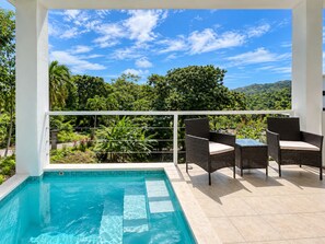 A pool area with a clear view of a mountainous landscape, surrounded by lush greenery.