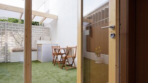 A patio area with a wooden table and chairs, a white fence, and a small garden with artificial grass. - Apartamento estudio con terraza-pensión* (A Estrada)