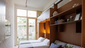 A modern room with two beds, a sofa, a dining table with a bowl of flowers, and a bookshelf. - Apartamento estudio con terraza-pensión* (A Estrada)