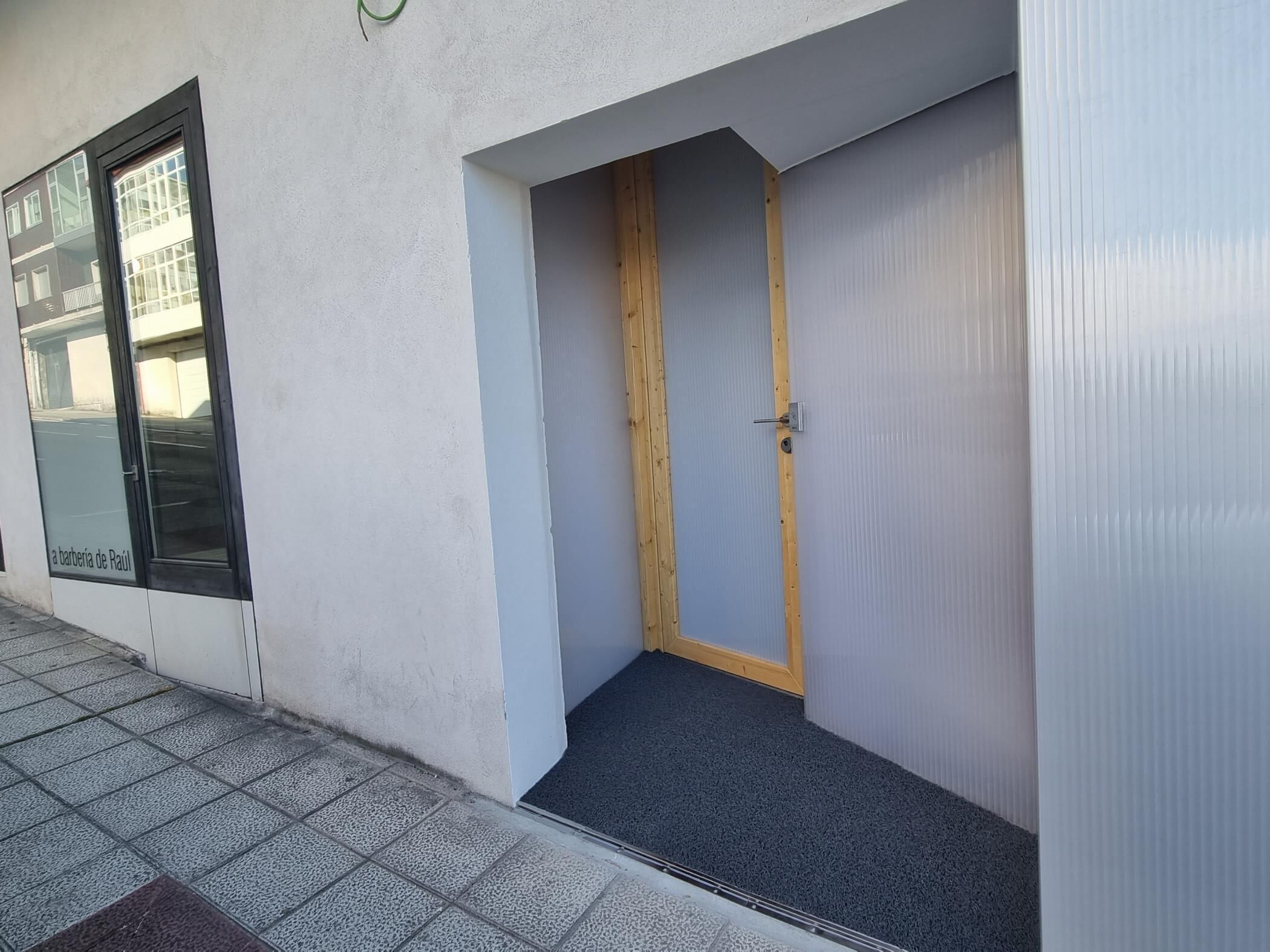 Een gebouwtrakt met een glazen deur, een kleine houten deur en een betegelde vloer.