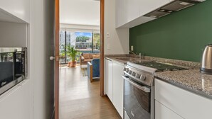 Une cuisine moderne équipée d’une cuisinière, d’un four et d’un plan de travail en granit. On aperçoit un coin repas avec une table et des chaises à travers une porte ouverte.