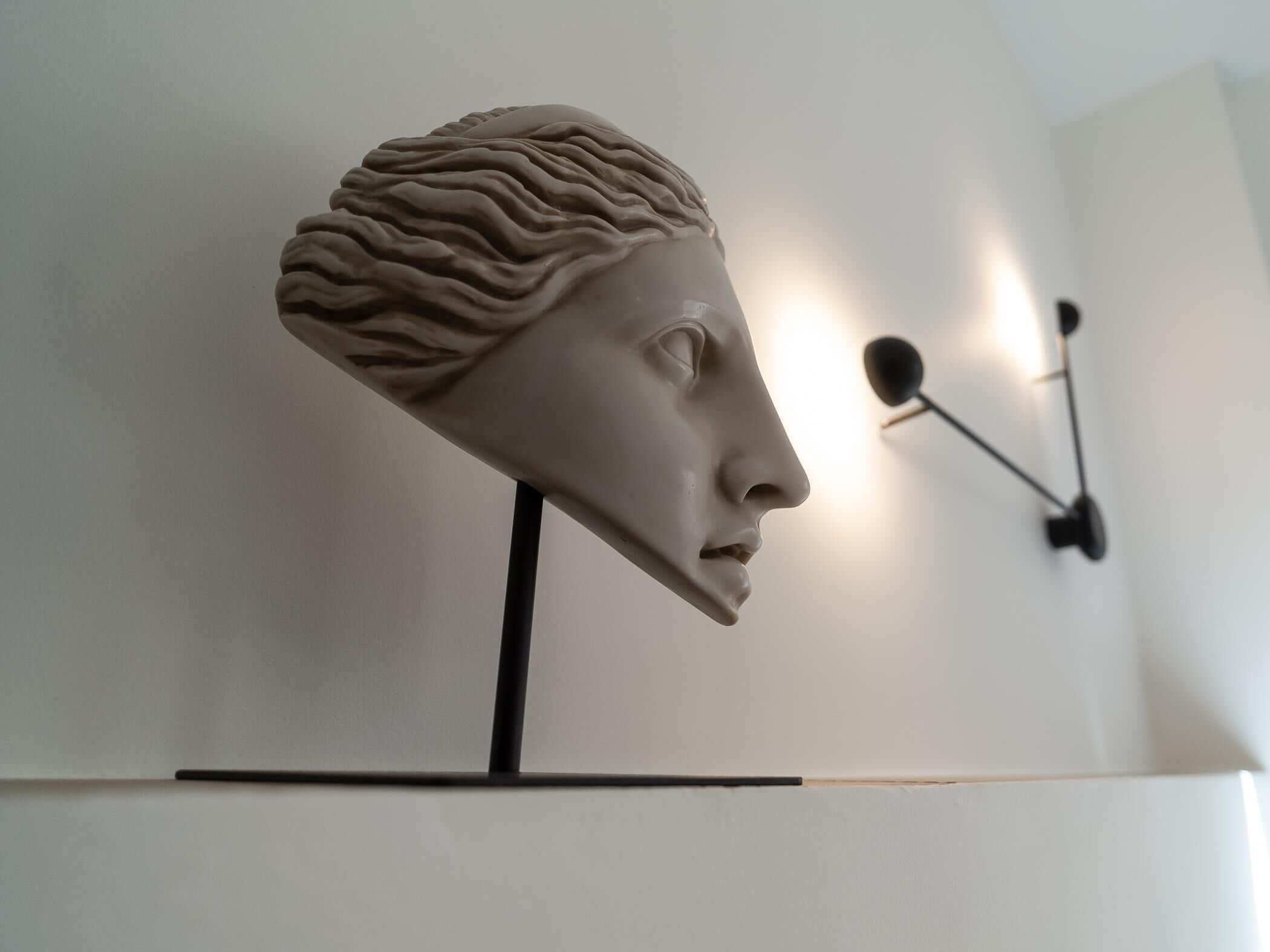 Eine Büstenstatue auf einem schwarzen Sockel vor einer weißen Wand.
