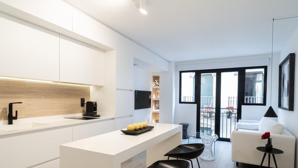 Una cocina moderna con encimera blanca, taburetes negros y una cafetera.
