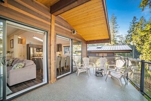 Une maison moderne dotée d’un balcon agrémenté de chaises Adirondack blanches et d’une porte vitrée donnant sur un salon avec un canapé et un coin repas.