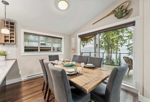 Un coin repas avec une table en bois, des chaises à revêtement gris et une vue sur les arbres à travers de grandes fenêtres.
