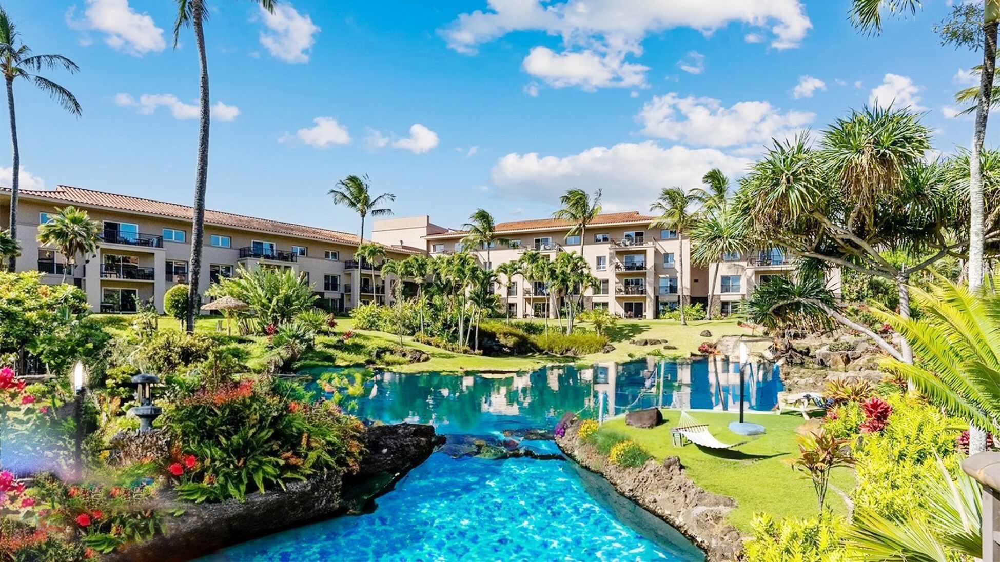 A resort with a swimming pool, palm trees, and a well-maintained lawn.