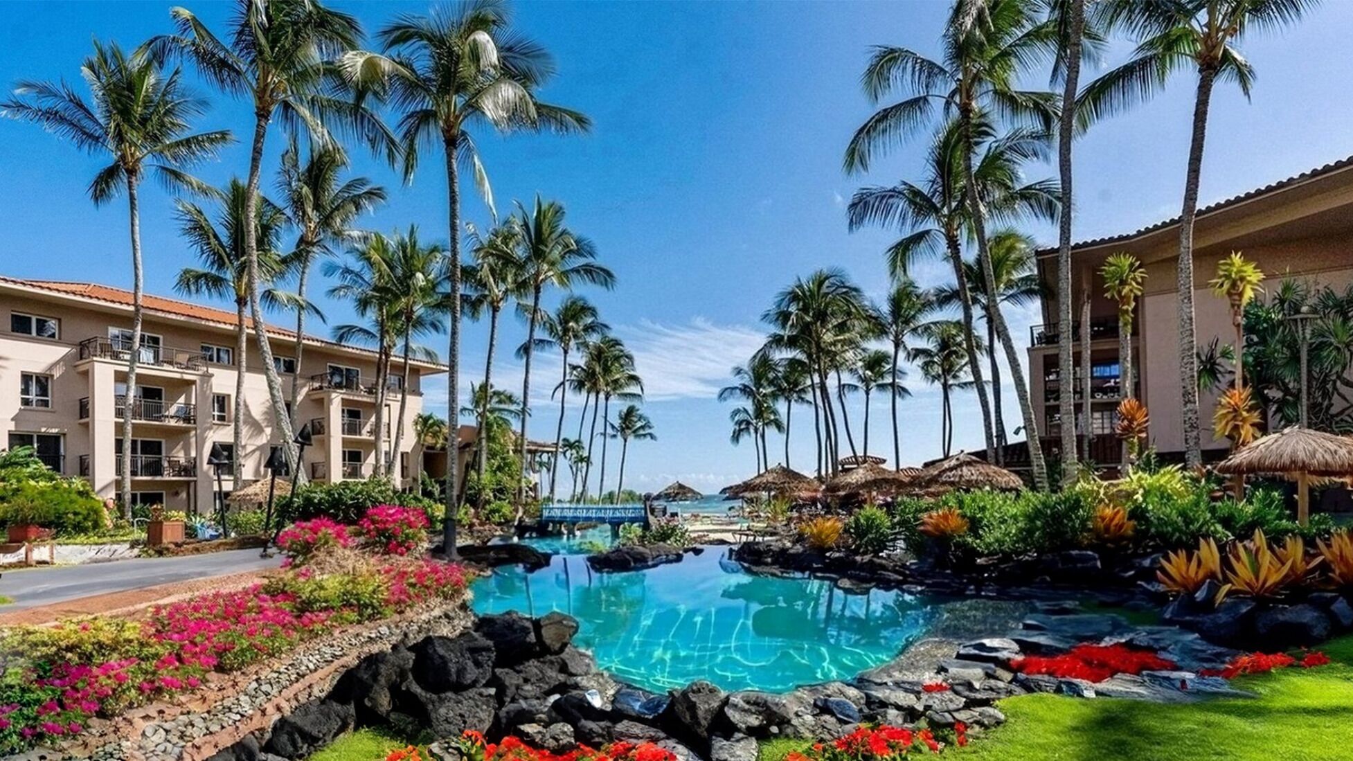 A resort with a central pool surrounded by palm trees and a beach.