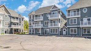 A row of multi-story buildings with balconies and a parking lot in front.