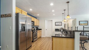 A modern kitchen with a stainless steel refrigerator, wooden cabinets, a built-in oven, and a bar area with a sink and stools.