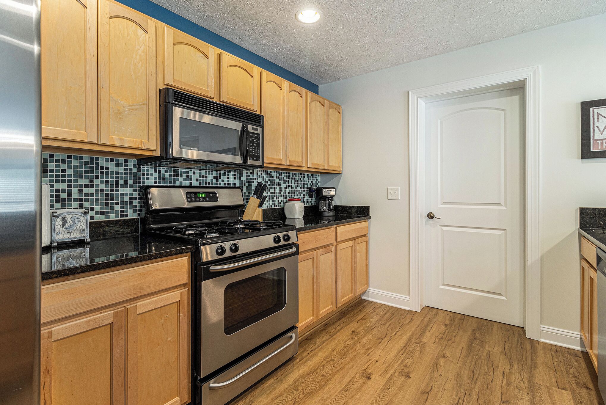 A kitchen with wooden cabinets, a stainless steel stove, a microwave, and a tiled backsplash.