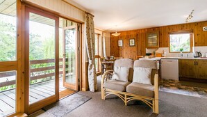 Interno di una baita in legno con zona pranzo, cucina e un balcone che si affaccia sul verde.