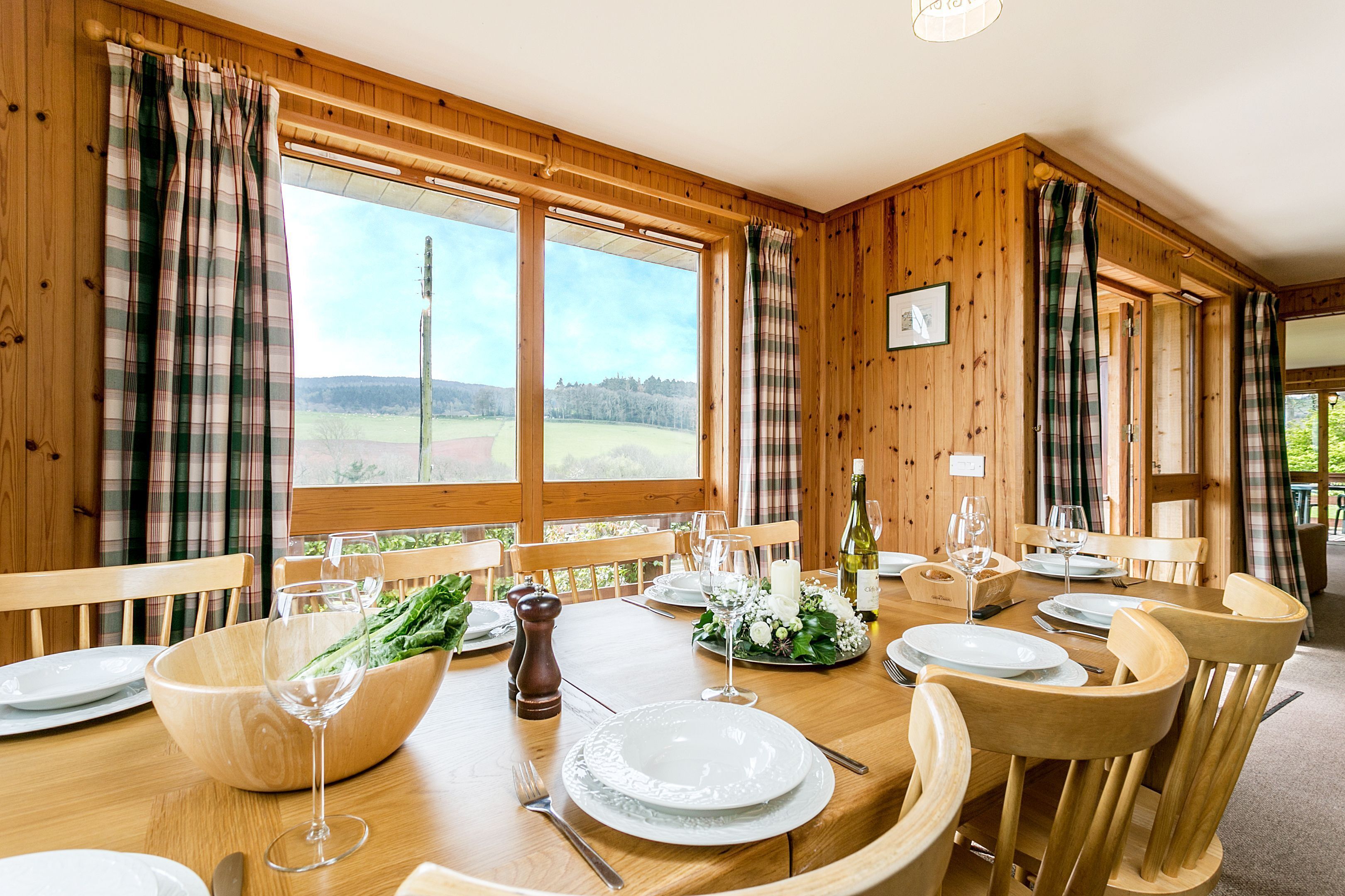 A wooden dining room with a large table set for a meal, large windows, and a view of the outdoors.