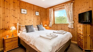 Ein Schlafzimmer mit Holzwandverkleidung, einem Bett, Nachttischen, einer Kommode, einem Fernseher und einem Fenster mit Vorhängen.