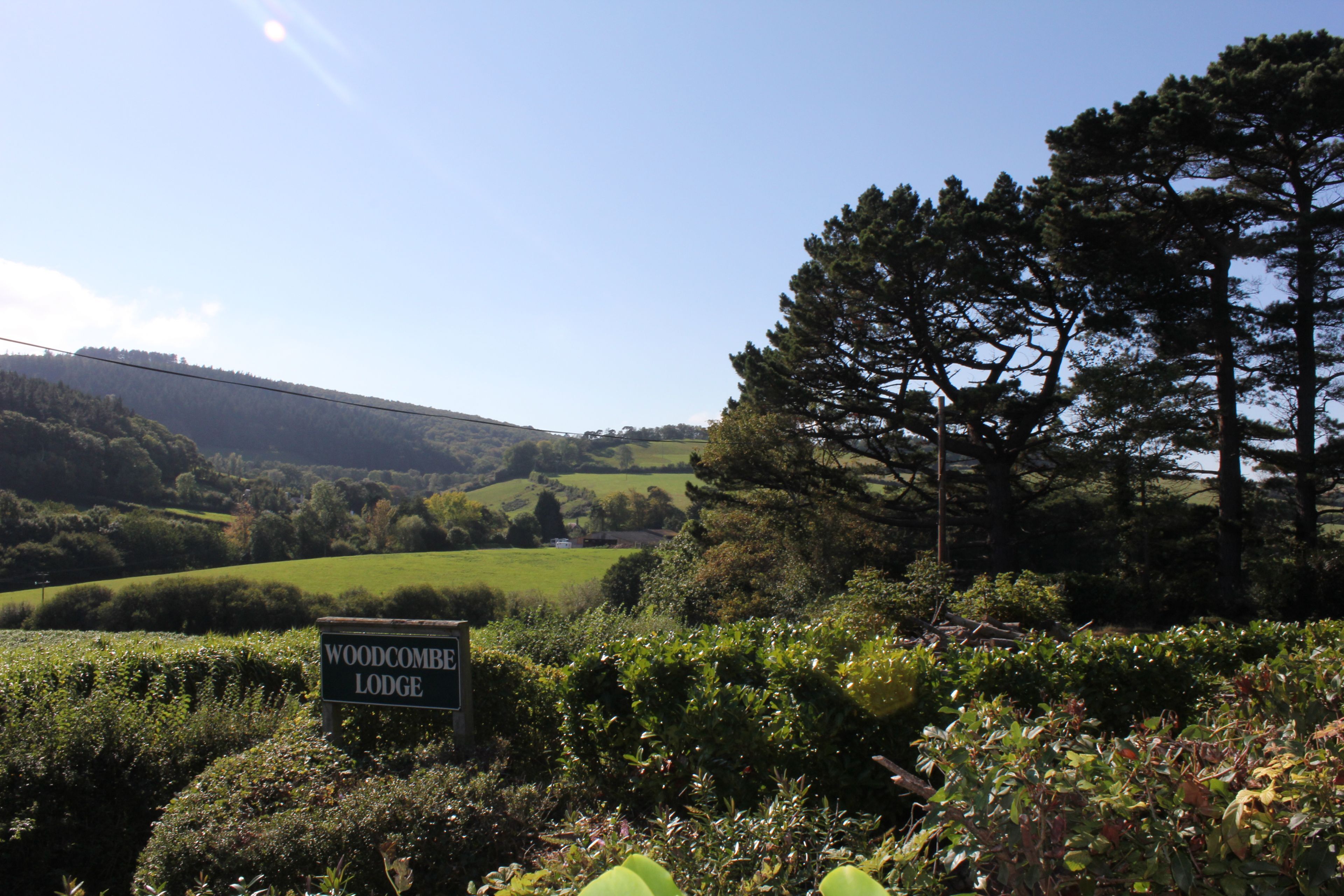 A sign for Woodcombe Lodge in a lush, green landscape with rolling hills and trees.