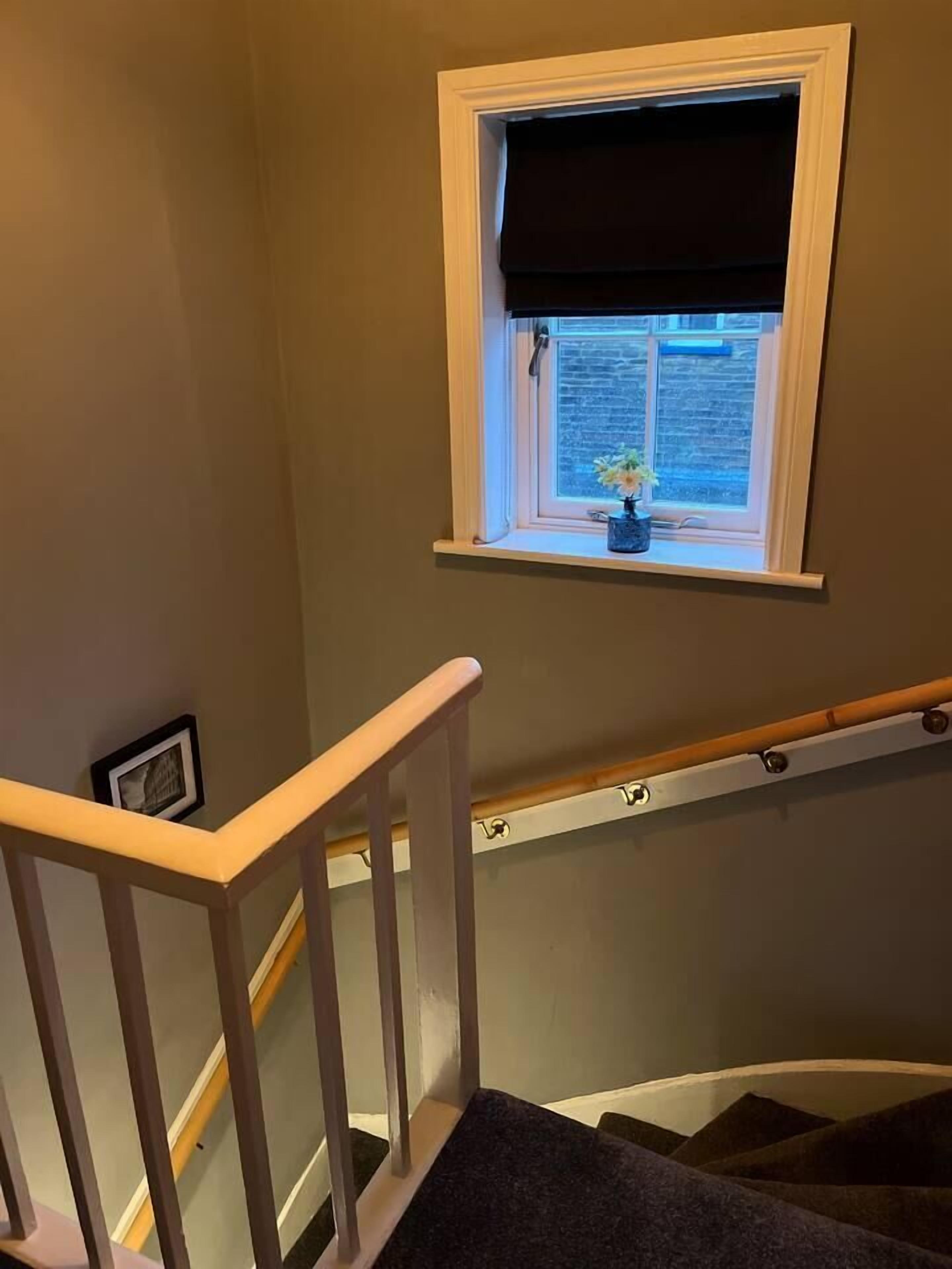 A staircase with a wooden handrail, a window with a dark blind, and a small potted plant on the windowsill.