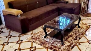 Een woonkamer met een bruine bank, een glazen salontafel en vloertegels met een patroon.