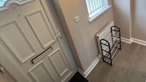 A hallway with a white door, a window with blinds, a radiator, and a black mat. - 1-Bed House, Sleeps 4, Free Parking (Stockport)
