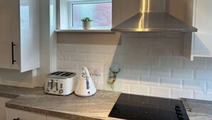 A kitchen with white cabinets, a stainless steel range hood, a toaster, a kettle, and a small potted plant on a window sill. - 1-Bed House, Sleeps 4, Free Parking (Stockport)
