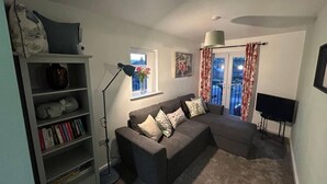 A living room with a grey sofa, a bookshelf, a floor lamp, and a TV. - 1-Bed House, Sleeps 4, Free Parking (Stockport)