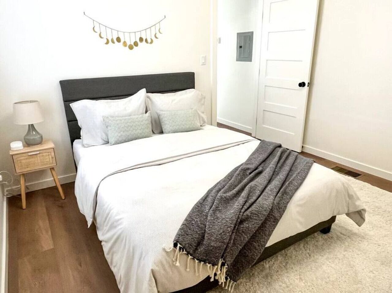 A neatly made bed with white linens and a gray throw blanket, a bedside table with a lamp, and a wall-mounted decoration.