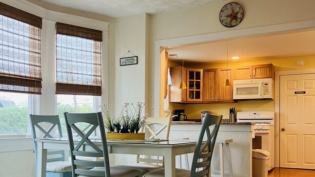 A dining area with a table and chairs, a ceiling fan, a kitchen with wooden cabinets, a microwave, and a trash can. - Cozy beach-inspired home! Close walk to boardwalk and beach! (Ocean City)
