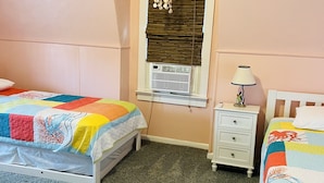 A bedroom with two beds, a window with blinds, a nightstand with a lamp, and a carpeted floor. - Cozy beach-inspired home! Close walk to boardwalk and beach! (Ocean City)