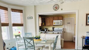 A cozy dining area with a white table and blue chairs, a kitchen with wooden cabinets, and a ceiling fan. - Cozy beach-inspired home! Close walk to boardwalk and beach! (Ocean City)