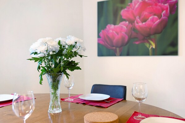 Une table à manger ornée d’un vase de fleurs blanches, d’une assiette et d’un verre à vin.