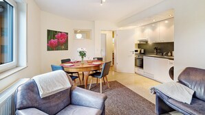 Ein modernes Wohnzimmer mit Esstisch, Sofas, Küchenzeile und großem Fenster.