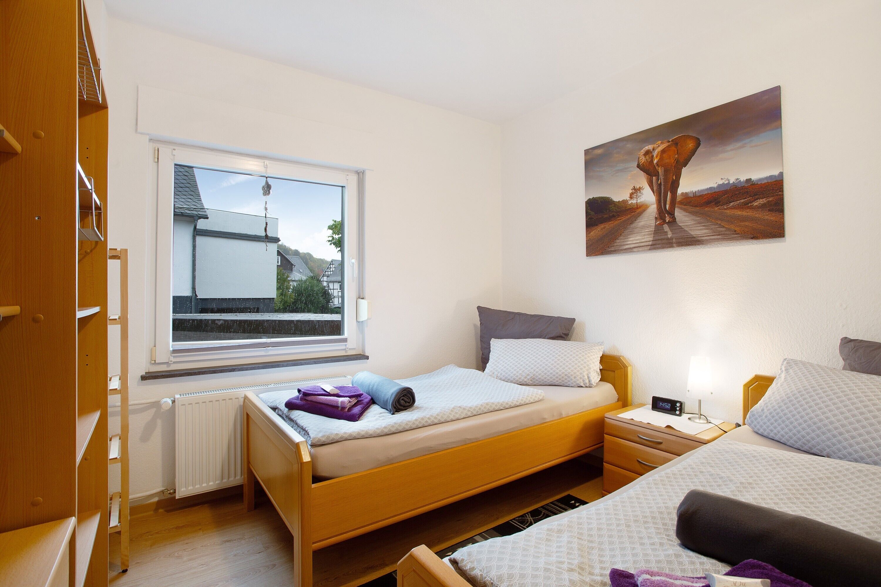 Ein Schlafzimmer mit zwei Betten, einem Fenster mit Blick, einem Bild an der Wand und einem Nachttisch mit Lampe.