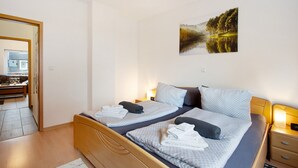 Ein Doppelbett mit zwei Kissen, ein Nachttisch mit Lampe und ein Waldbild an der Wand.