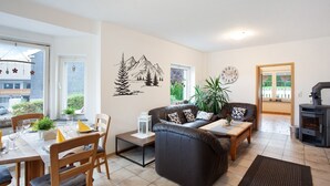 Ein Wohnzimmer mit Sofa, Sesseln, einem Esstisch, einem Kamin und Blick ins Freie.