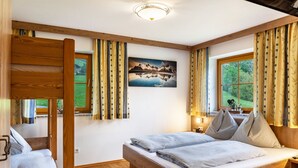 Ein Schlafzimmer mit einem hölzernen Bett, einem Fenster mit Vorhängen, einem Bild an der Wand und einem Etagenbett.