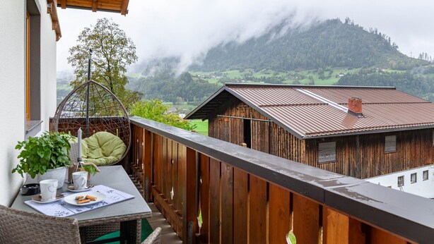 Ein Balkon mit Bergblick, einem Holzzaun und einem Tisch mit Pflanze und Tasse.