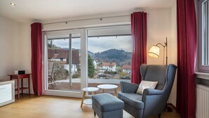 A modern living room with a grey armchair, a small ottoman, a white table, and a floor lamp. - Apartment 'Fewo Zeit Zu Zweit' with Mountain View, Private Terrace and Wi-Fi (Sasbachwalden)