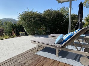 Een ligbed met kussen, een tafel met stoelen en uitzicht op een heuvel.