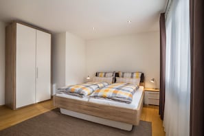 Une chambre à coucher comprenant un lit, des tables de chevet, une armoire et une fenêtre avec des rideaux.