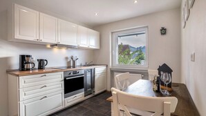 A kitchen with white cabinets, a wooden countertop, a dining table with chairs, and a window with a view. - Apartment 'Fewo Zeit Zu Zweit' with Mountain View, Private Terrace and Wi-Fi (Sasbachwalden)
